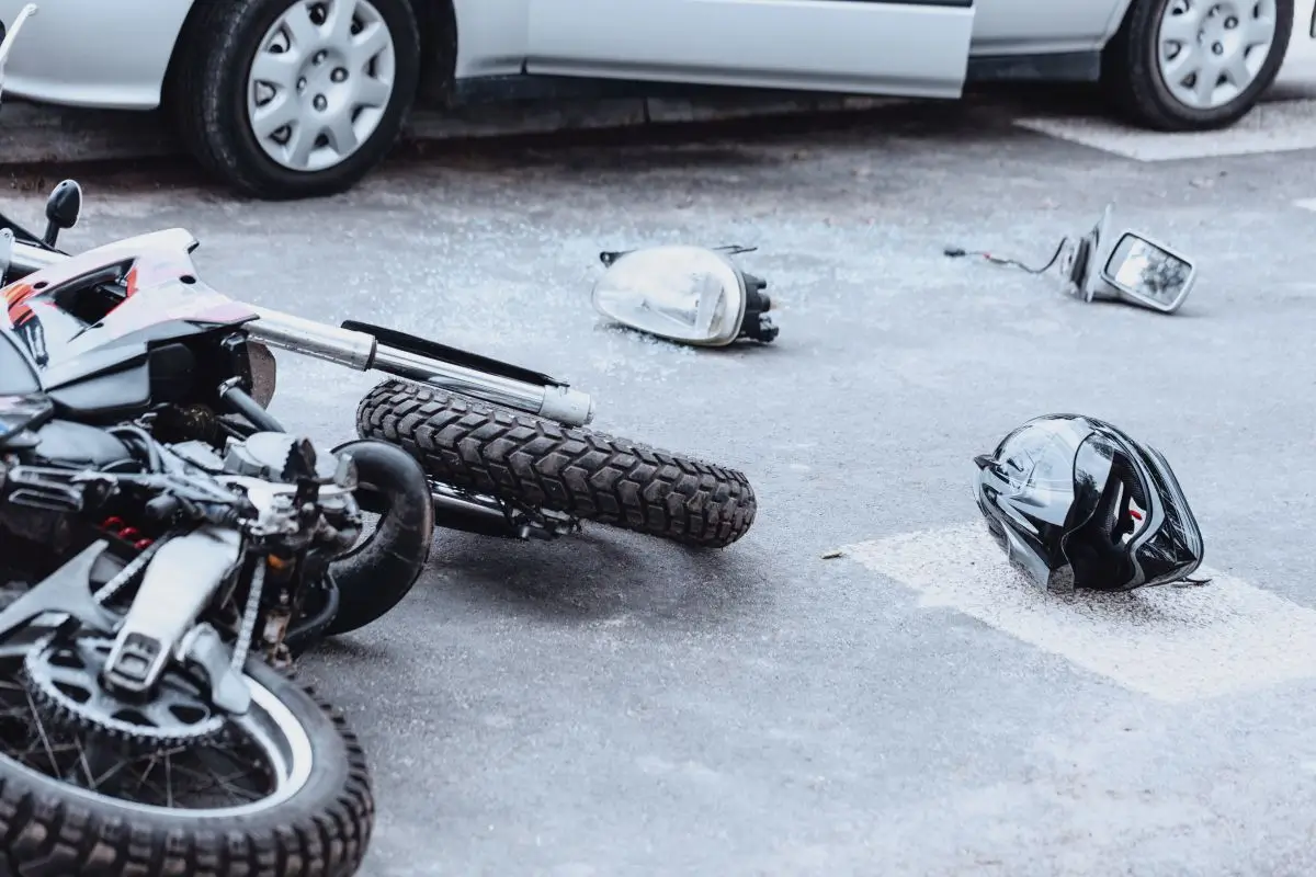 Damaged motorcycle and helmet lying on the road after a collision with a car, showing the aftermath of a motorcycle accident.