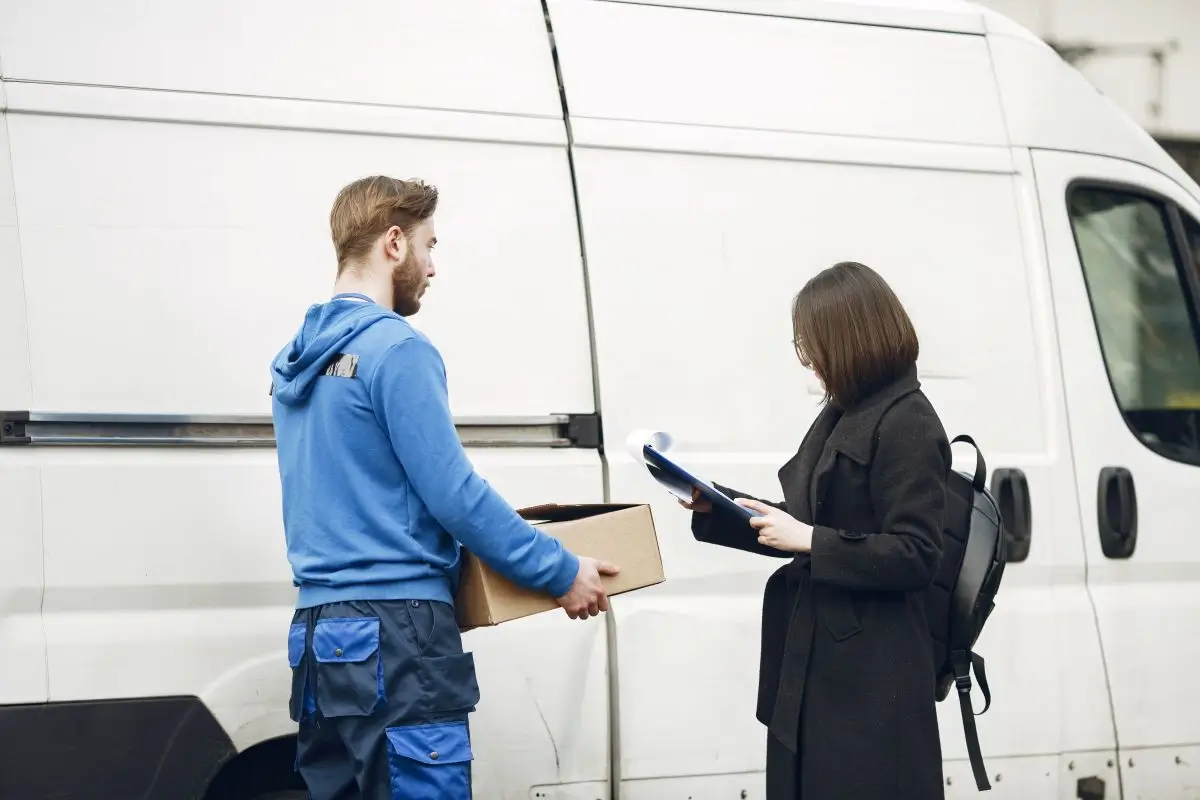 Delivery driver handing a package to a customer for signature beside a white van, representing potential delivery or workplace injury scenario.