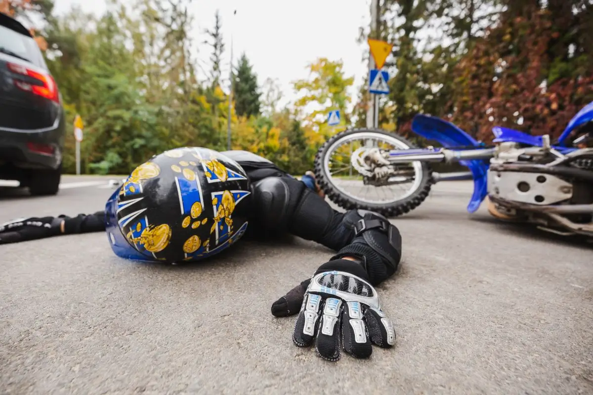 Injured motorcyclist lying on the road after a motorcycle accident, wearing protective gear and helmet near a fallen bike.