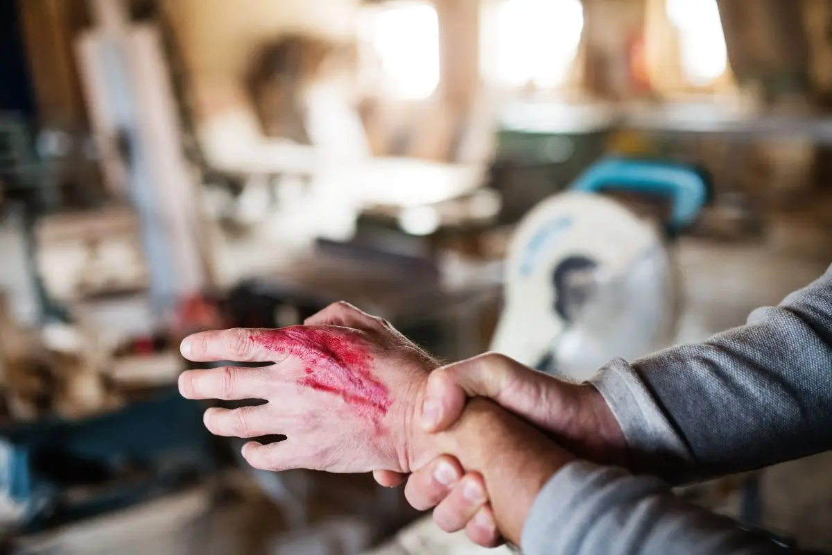 Worker holding an injured and bleeding hand after an accident in a workshop, symbolizing a workplace injury or workers’ compensation case.