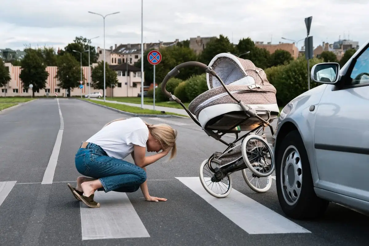 Distressed woman kneeling on a crosswalk near a baby stroller after a car accident.