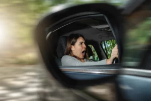 Woman visible in a car side mirror with a surprised expression, blurred background suggesting motion and urgency — evoking shock, alarm, and the possibility of a car accident for a partial-fault injury claim.