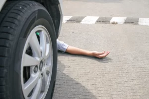 Person’s arm trapped beneath a vehicle wheel after a serious roadway accident, illustrating injuries that may lead to a company vehicle accident lawsuit in Massachusetts.